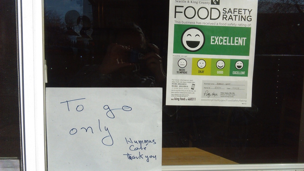 March 23, 2020, Greenwood, Seattle. In the window of a local restaurant, a food safety rating sheet is displayed as required by law. This one has an "excellent" rating, which is the highest of four ratings. Next to the food safety rating sheet is a hand-written sign that says "To go only" and, in the bottom right corner, "Hummus Cafe," and below that, "Thank you."