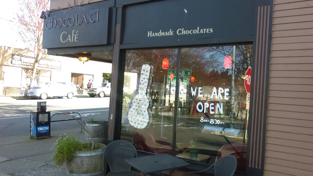 March 23, 2020, Greenwood, Seattle. Big hand-written letters on the windows of Chocolati cafe read "WE ARE OPEN."